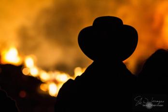 Silhouette of a man in a hat, against a backdrop of roaring flames from a communal bonfire, part of the annual tradition known as Fireworks Night, Bonfire Night or Guy Fawkes Night, across the UK. For the week around November 5th, bonfires are lit and fireworks released to commemorate the foiling of the 1605 Gunpowder Plot, against the Parliament of King James I.